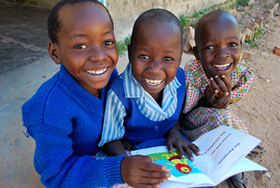 Girls share a book and smiles outside of their classroom at Matau Primary School in Zimbabwe. May 4, 2011. Photo Credit: Eileen Burke/Save the Children