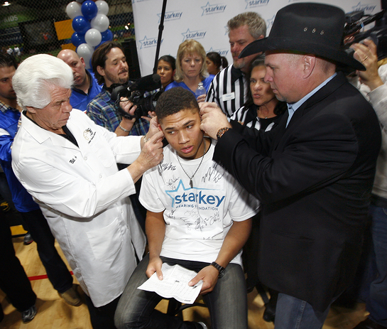 Garth Brooks assists Bill Austin, CEO and Founder, Starkey Hearing Foundation, fit an Indiana teen with digital, custom made hearing aids.