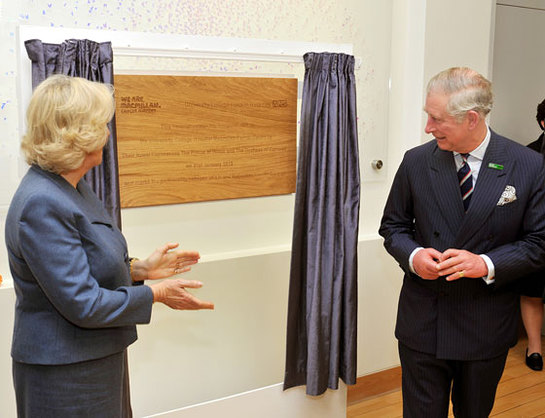 The Prince of Wales and the Duchess of Cornwall admire a wooden plaque unveiled by the Prince, during a tour of the new Macmillan Cancer Support unit 